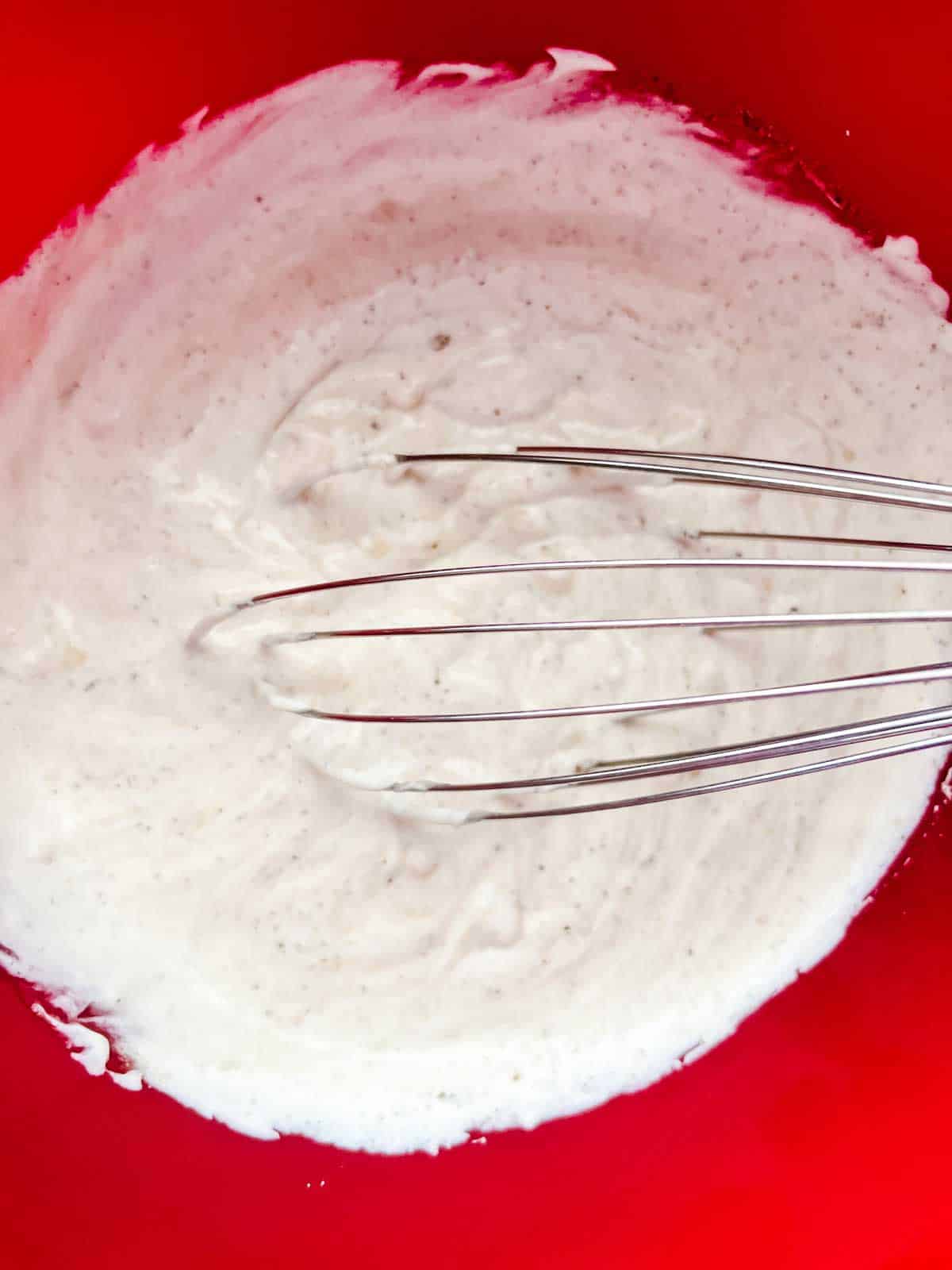 Photo of chicken soup, sour cream, garlic powder, salt, and pepper being whisked together in a bowl.