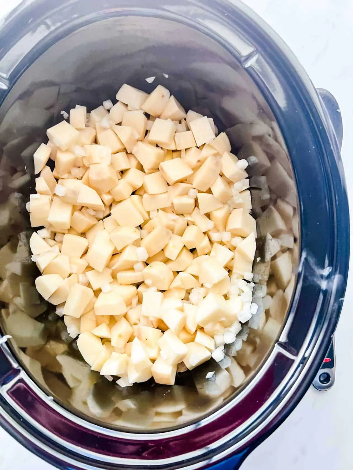 Photo of diced onion and potatoes that have been stirred together in a slow cooker.