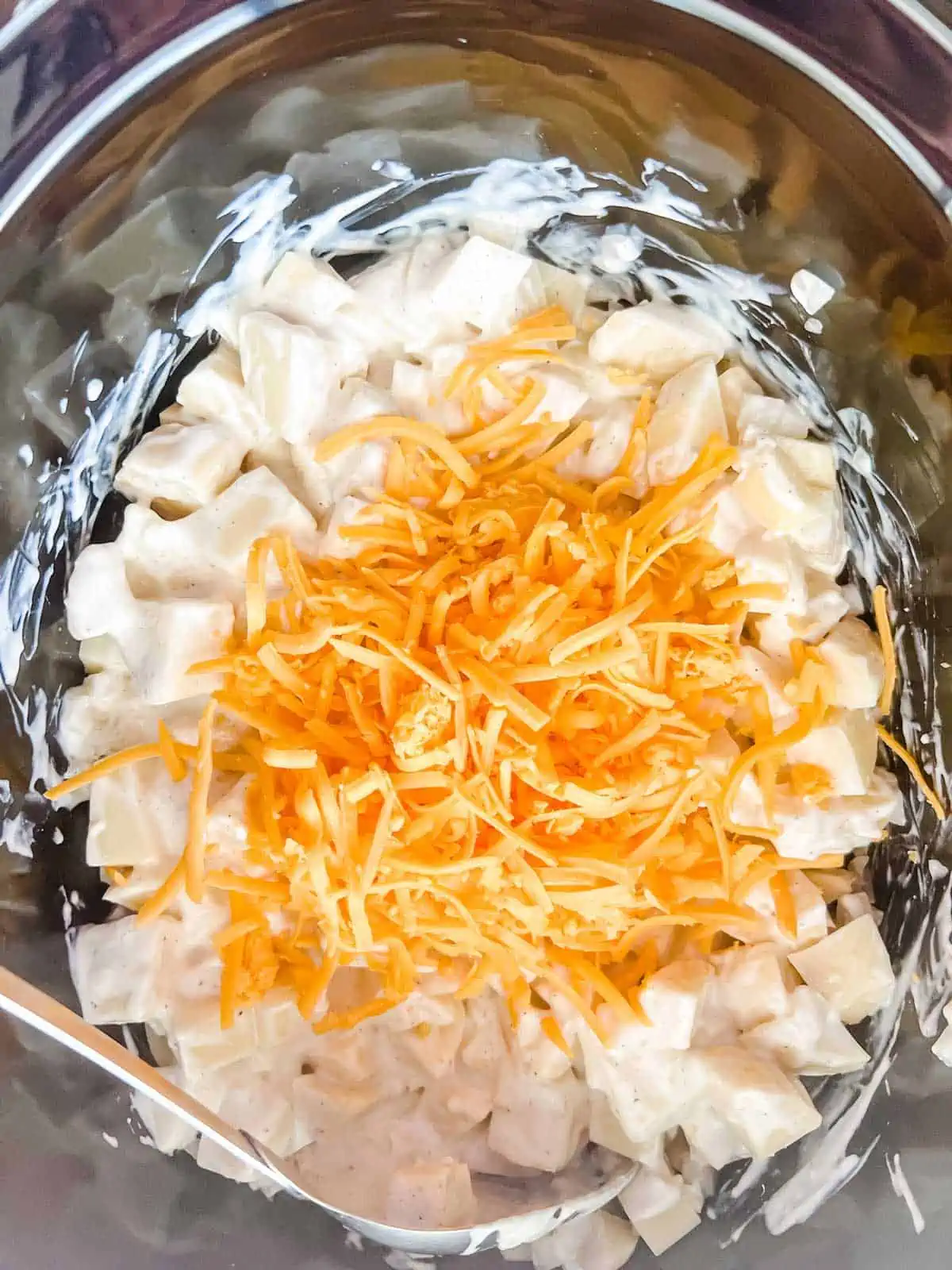 Photo of potatoes with shredded cheddar cheese in a crockpot.