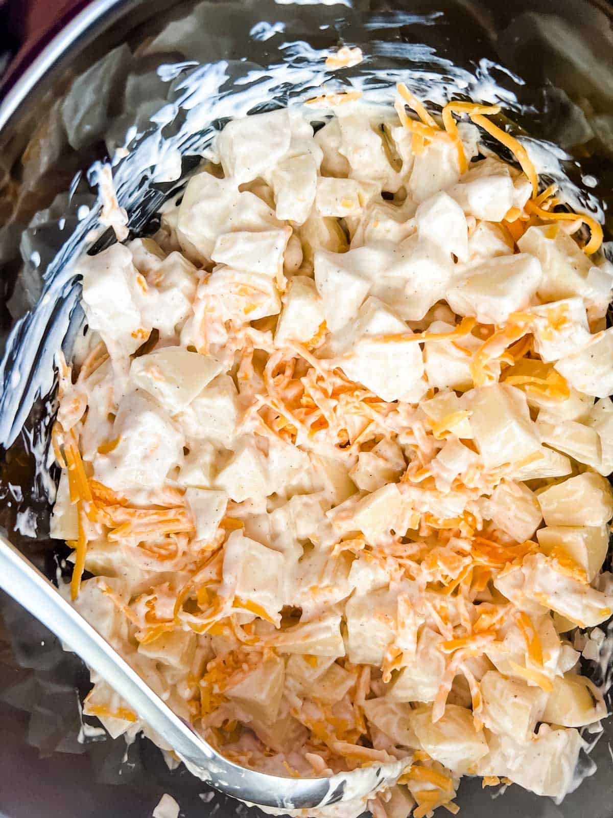 Photo of creamy potatoes with shredded cheese in a slow cooker ready to cook.