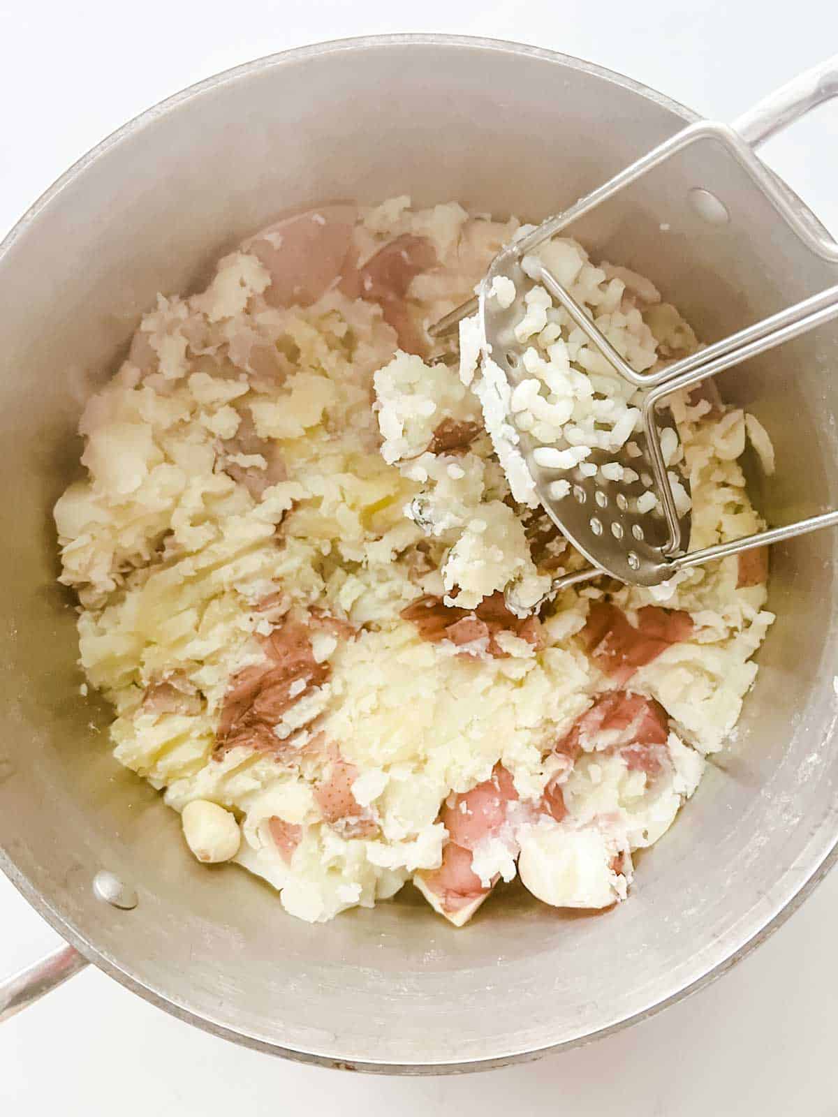 Photo of red potatoes being mashed with a potato masher.