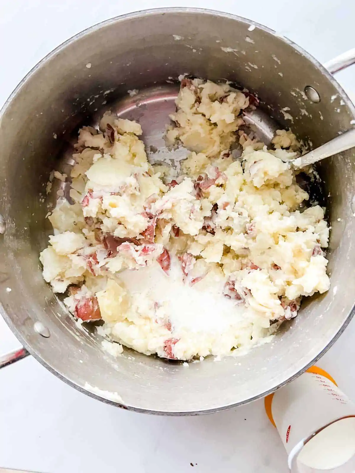 Photo of milk being added to mashed red potatoes.