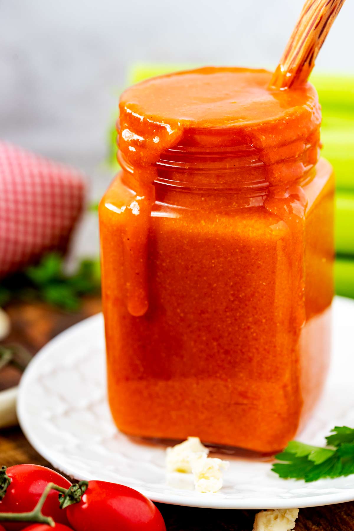Side photo of a glass jar with homemade buffalo sauce in it and drizzling down the side.