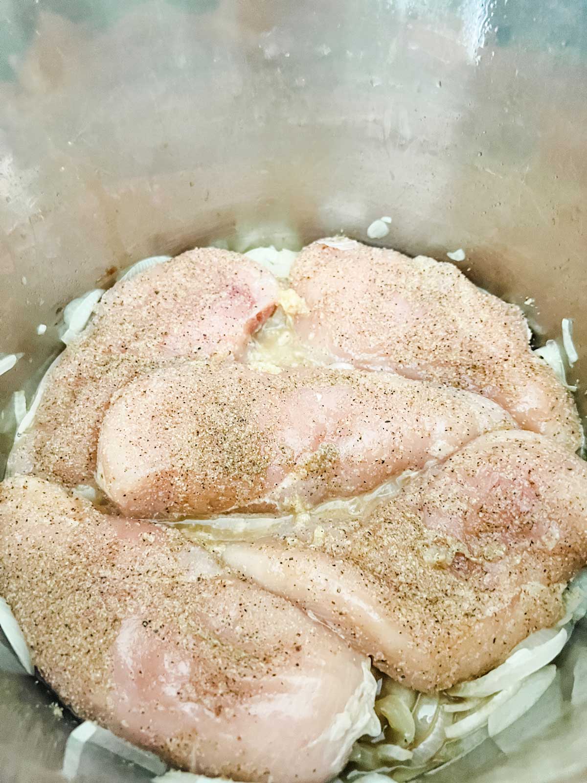 Photo of chicken breasts on top of onions in a pressure cooker.
