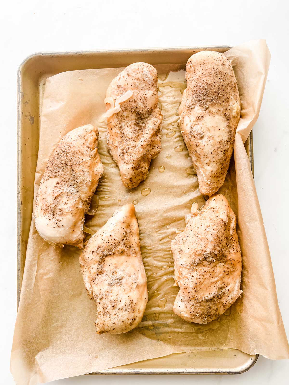 Chicken on a parchment lined baking sheet.