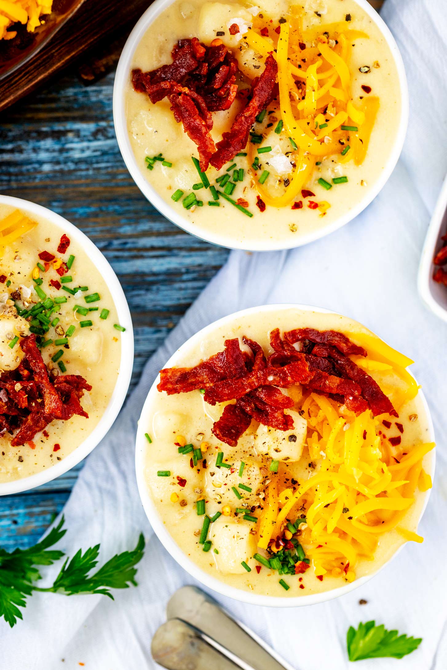 Overhead photo of three small bowls of Ninja Foodi Potato Soup garnished with bacon, shredded cheese, and chives.