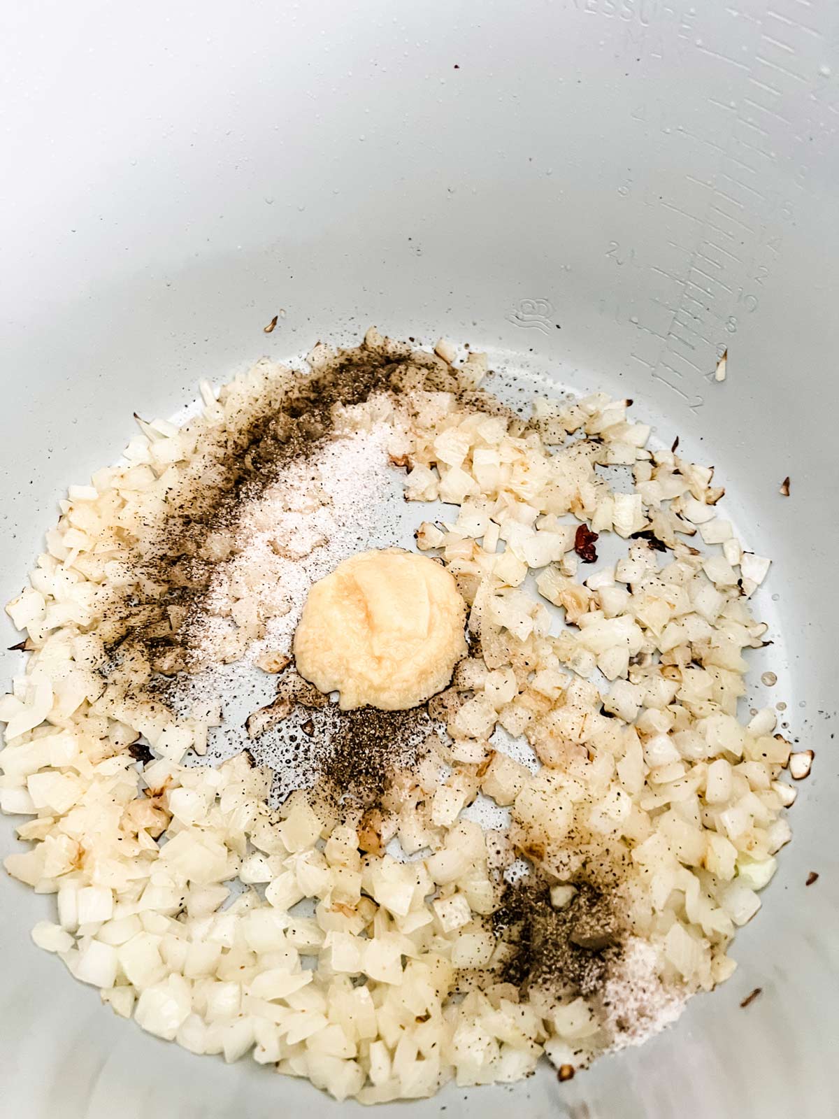 Overhead photo of onion, garlic, and seasonings cooking in a Ninja Foodi.
