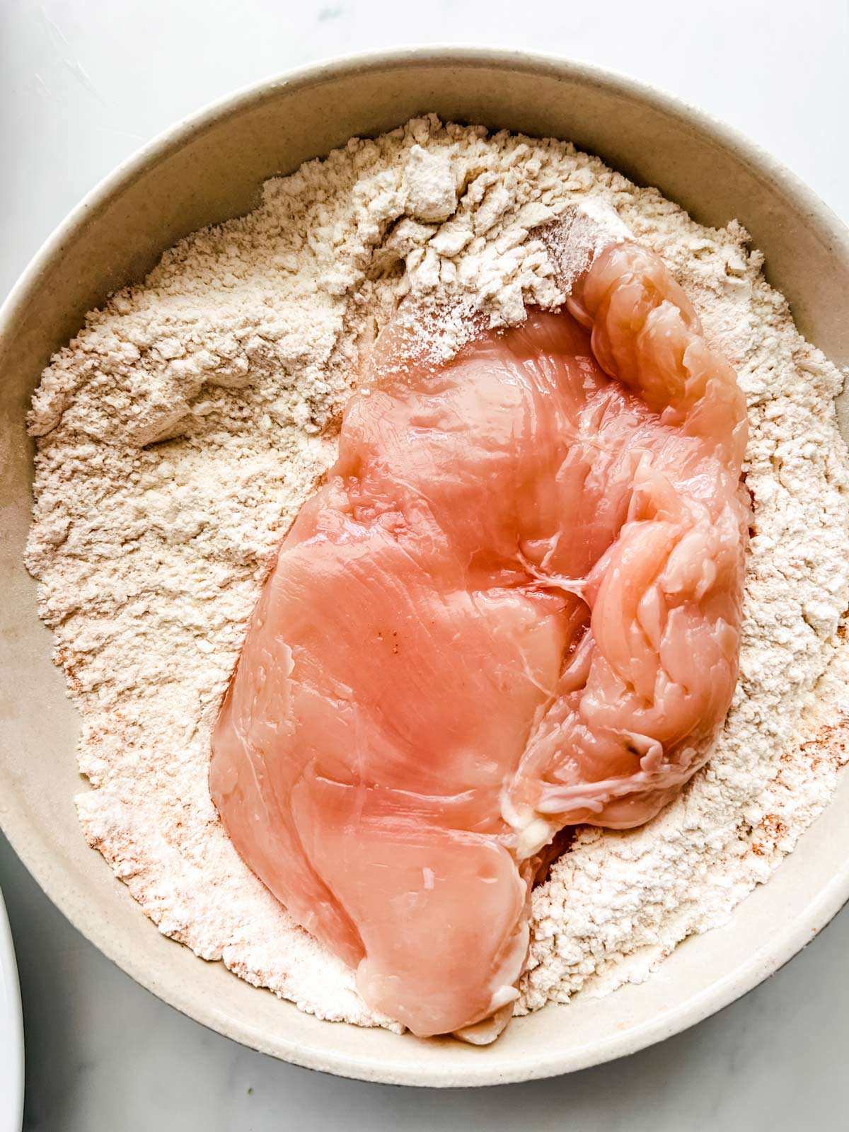 Chicken being dredged in a bowl of flour and seasonings.