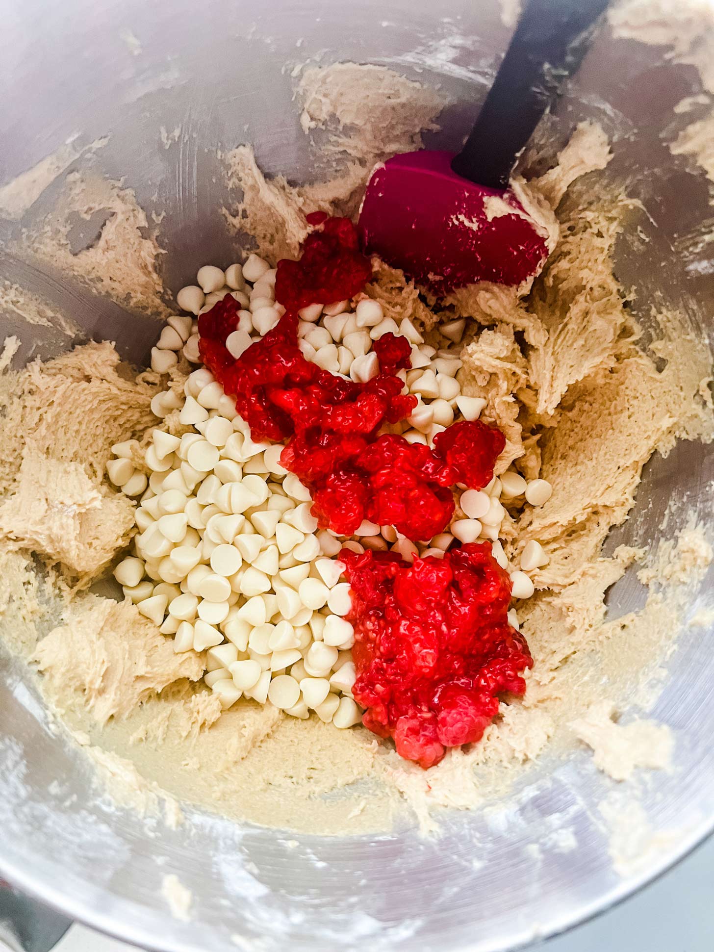 Photo of raspberries and white chocolate that have just been added to cookie dough. 