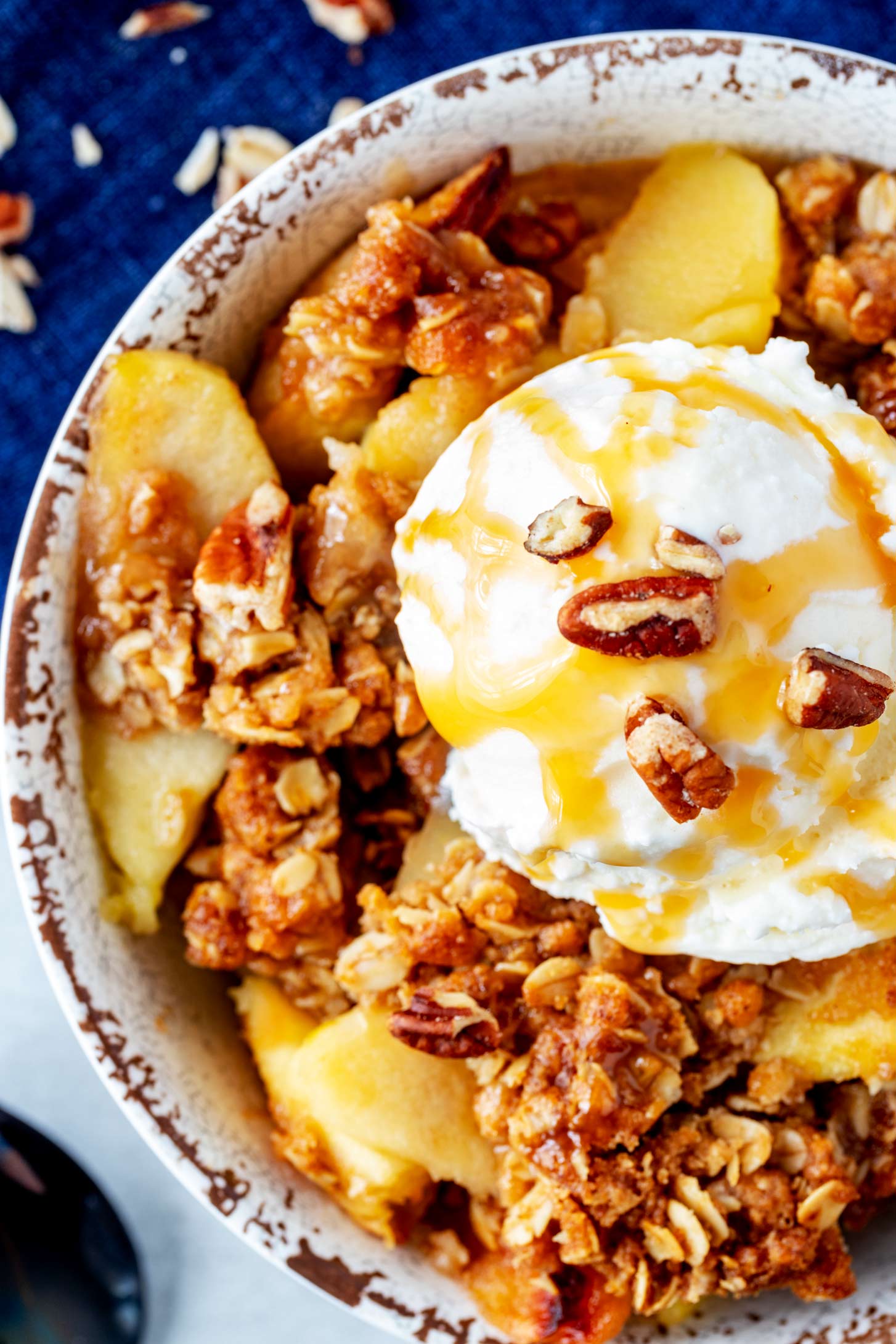 Close up overhead photo of a Ninja Foodi Apple crisp in a rustic bowl garnished with ice cream, caramel, and pecans.