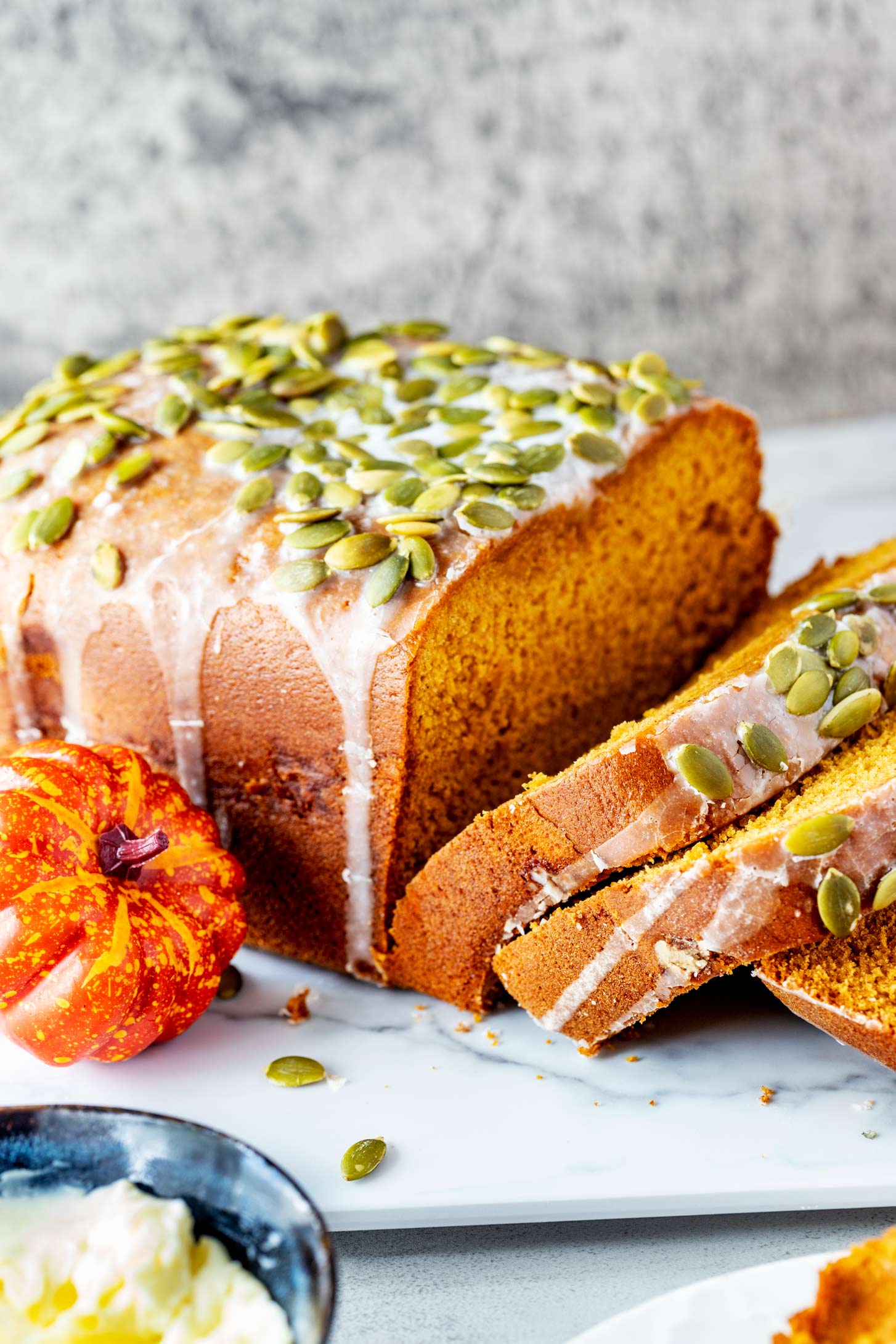 Side photo of a partially sliced loaf of bread machine pumpkin bread with a small pumpkin and pumpkin seeds next to it.