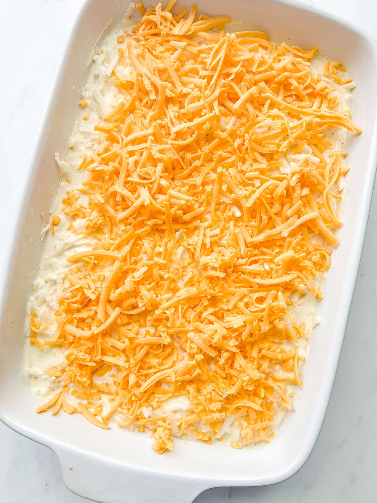 Cheddar cheese topped hash brown casserole ready for the oven.