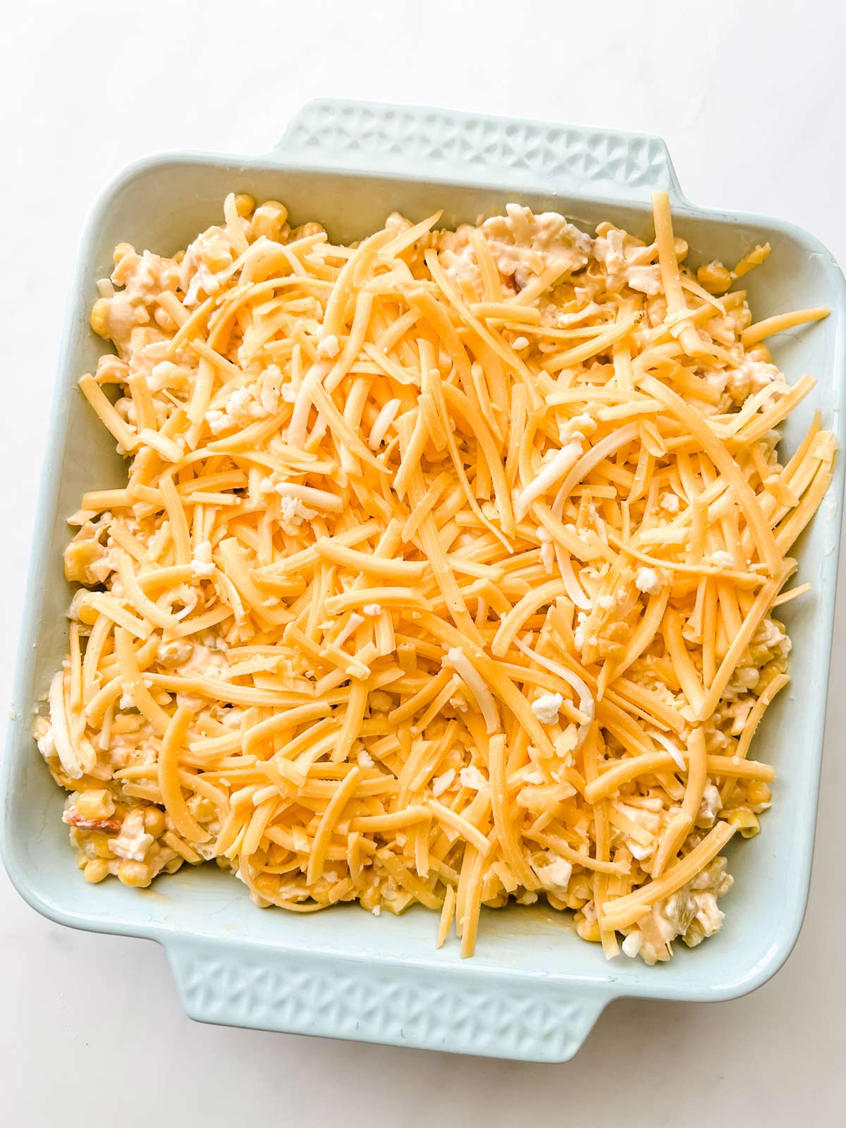 Shredded cheddar cheese on top of corn dip in a casserole dish.