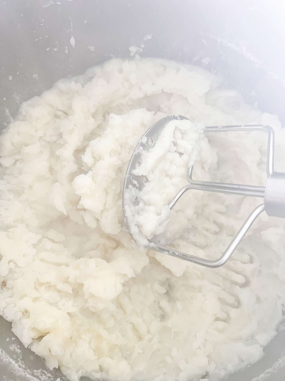 Potatoes and butter being mashed with a potato masher.