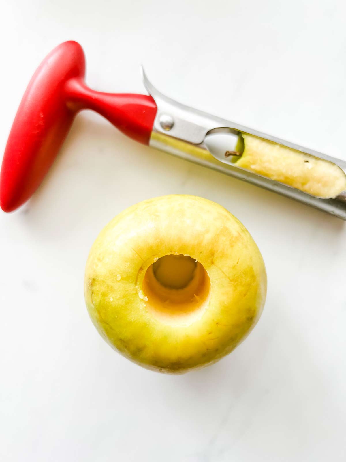 Photo of a cored apple with an apple corer sitting next to it.