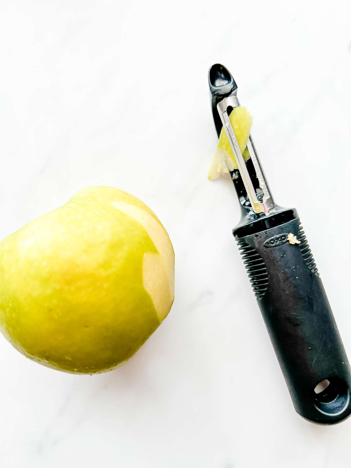 Photo of an apple with a peeler next to it.