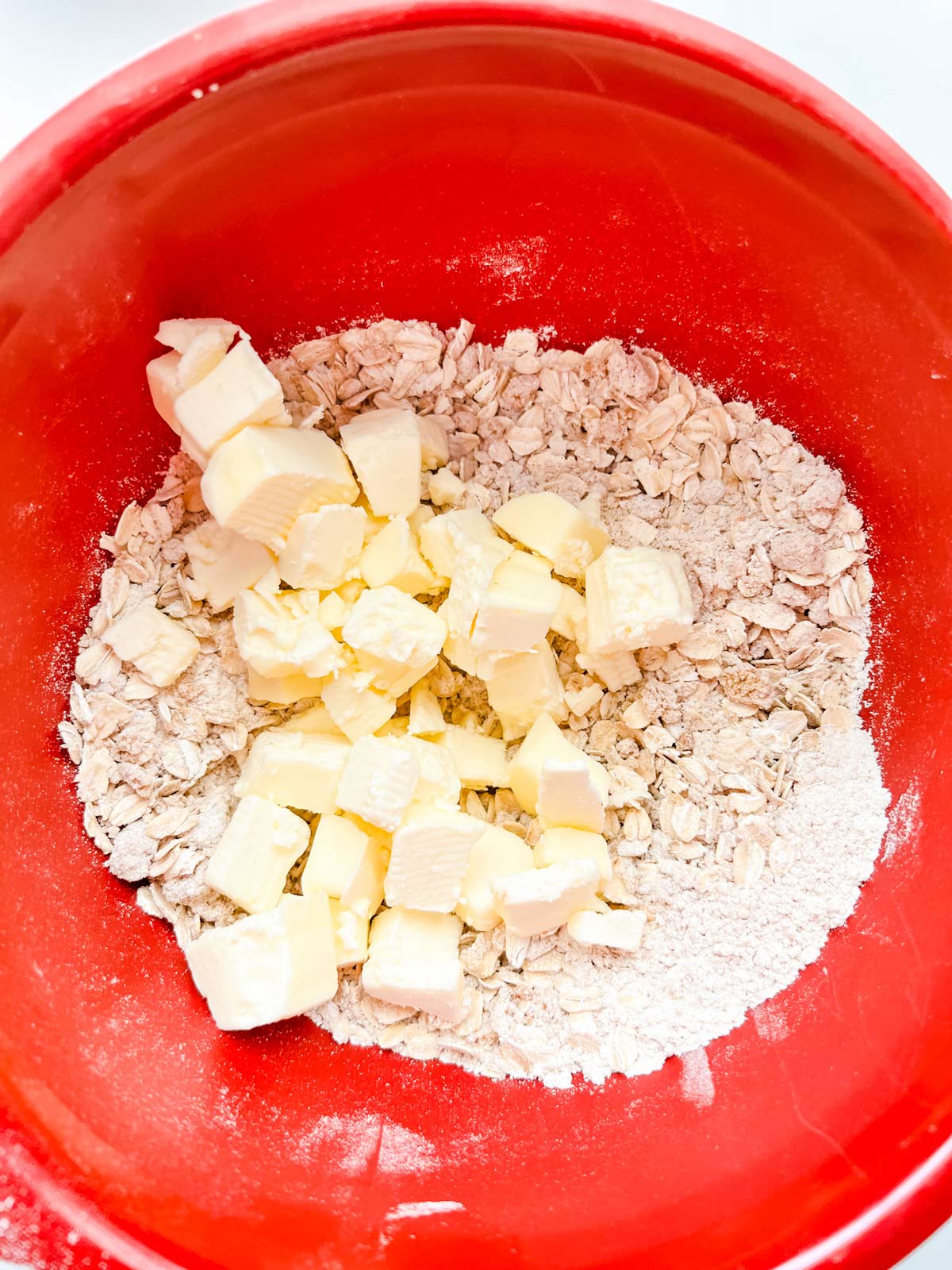 Photo of cubed butter on top of oats, flour, and brown sugar in a red bowl.