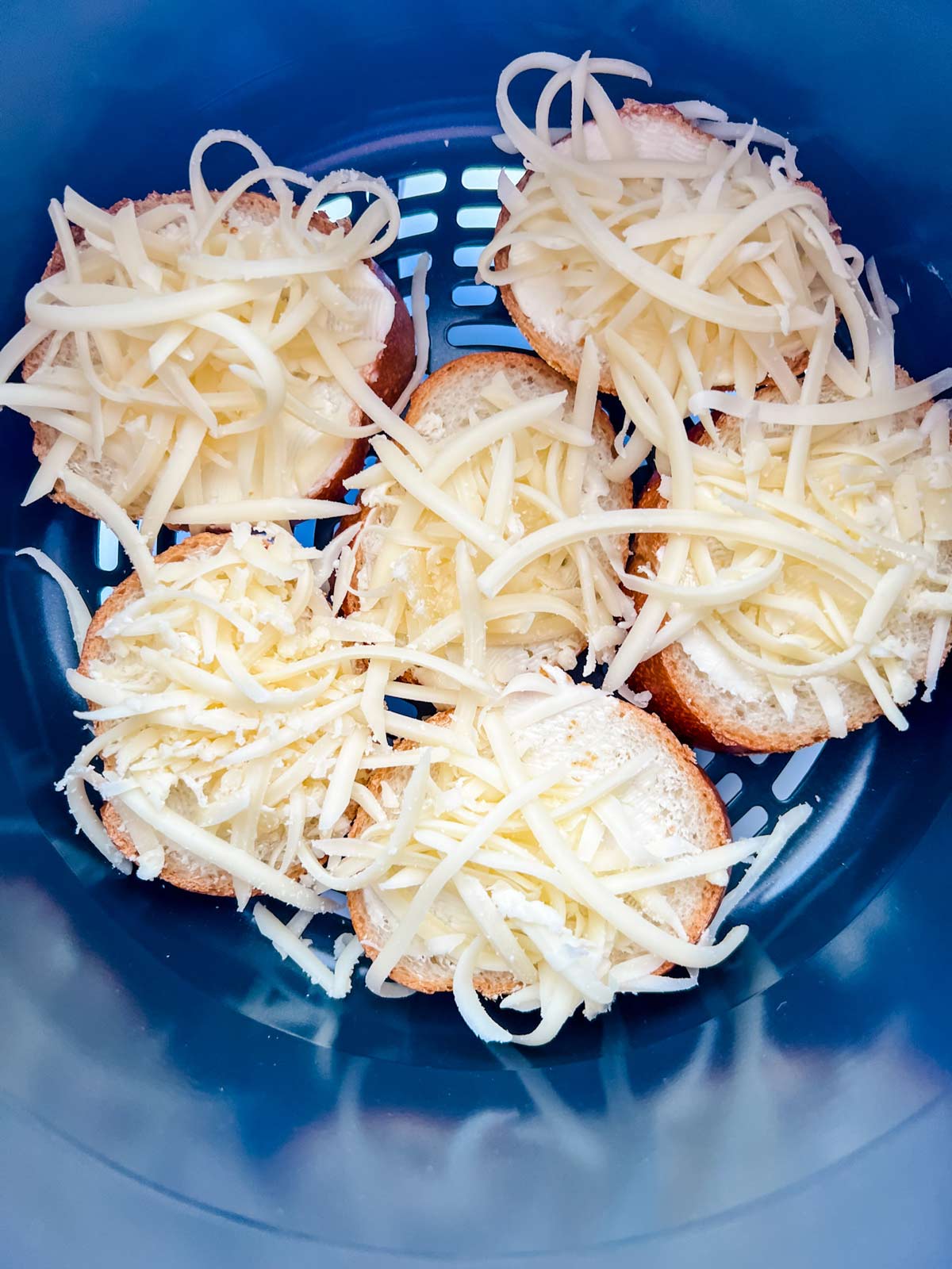 Buttered toast with cheese on top in an air fryer basket for a Ninja Foodi.