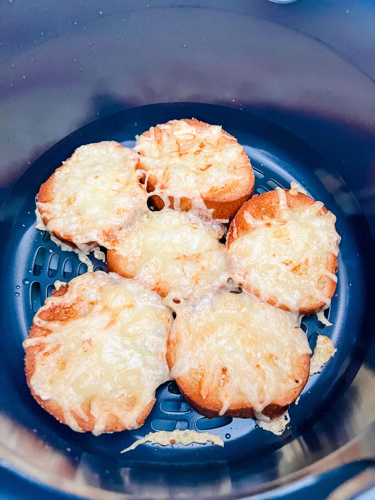 Cheesy toasted french baguettes in a Ninja Foodi air fryer basket.