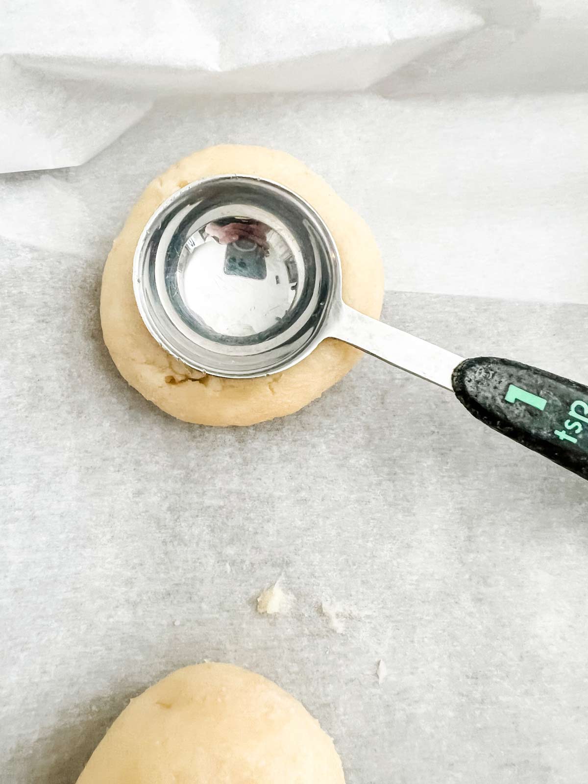 Uncooked thumbprint cookie dough having an indent made in it with a teaspoon measure.