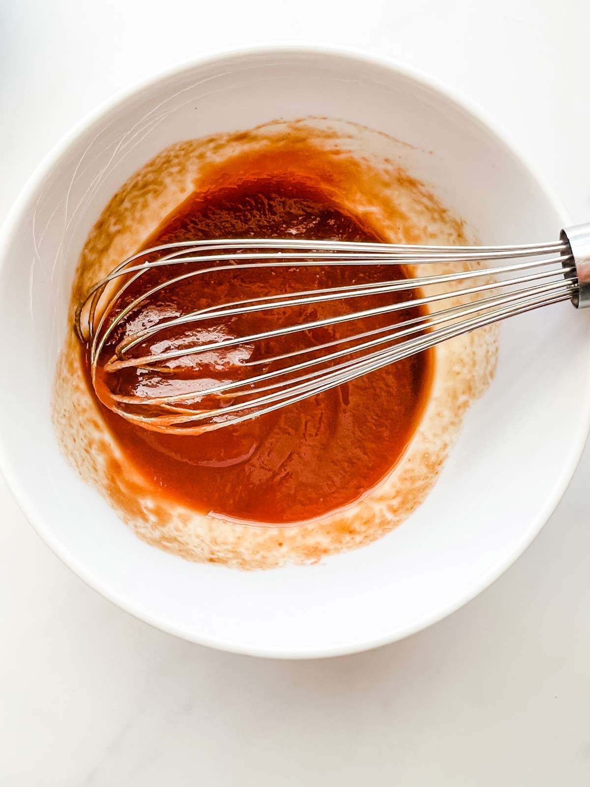 Meatloaf glaze being whisked together in a small white bowl.
