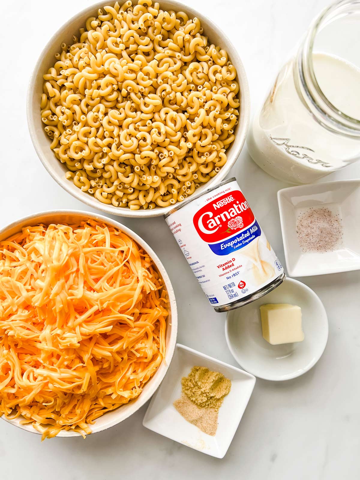 Overhead photo of elbow noodles, milk, evaporated milk, salt, butter, cheese, mustard powder, and garlic powder.
