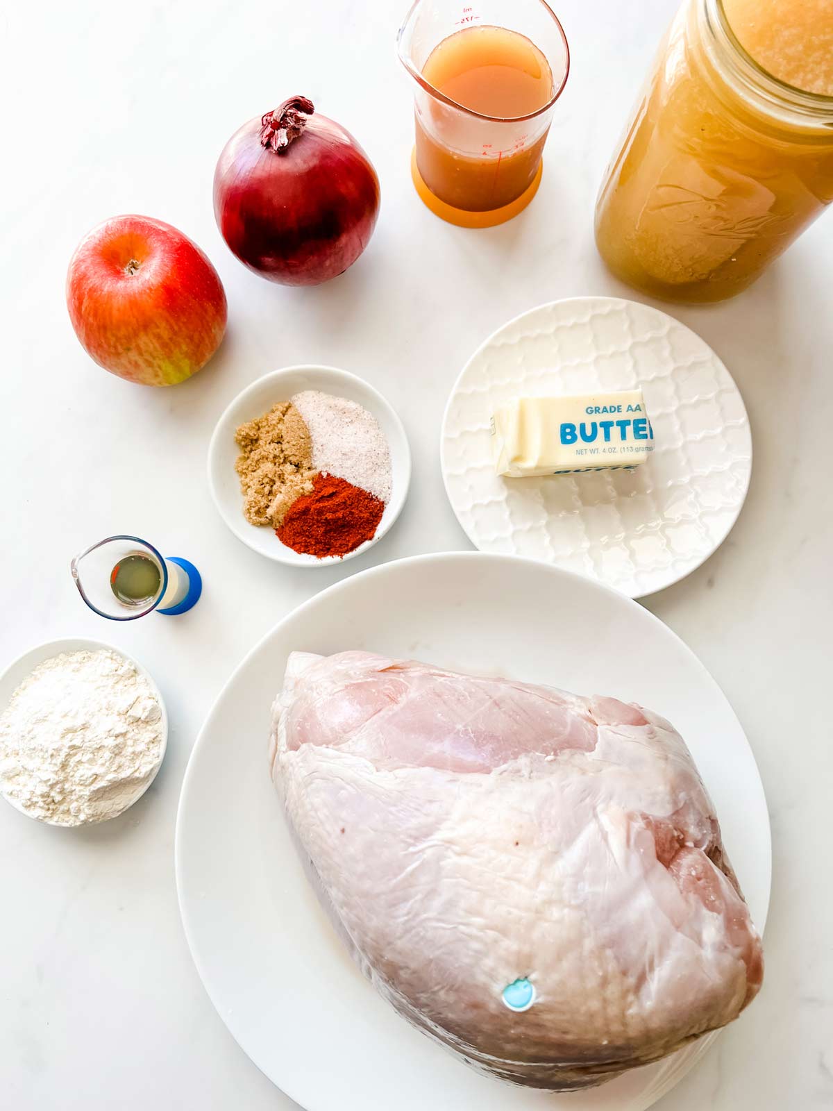 Overhead photo of a turkey breast, broth, apple cider, apple cider vinegar, onion, apple, seasonings, and cornstarch.
