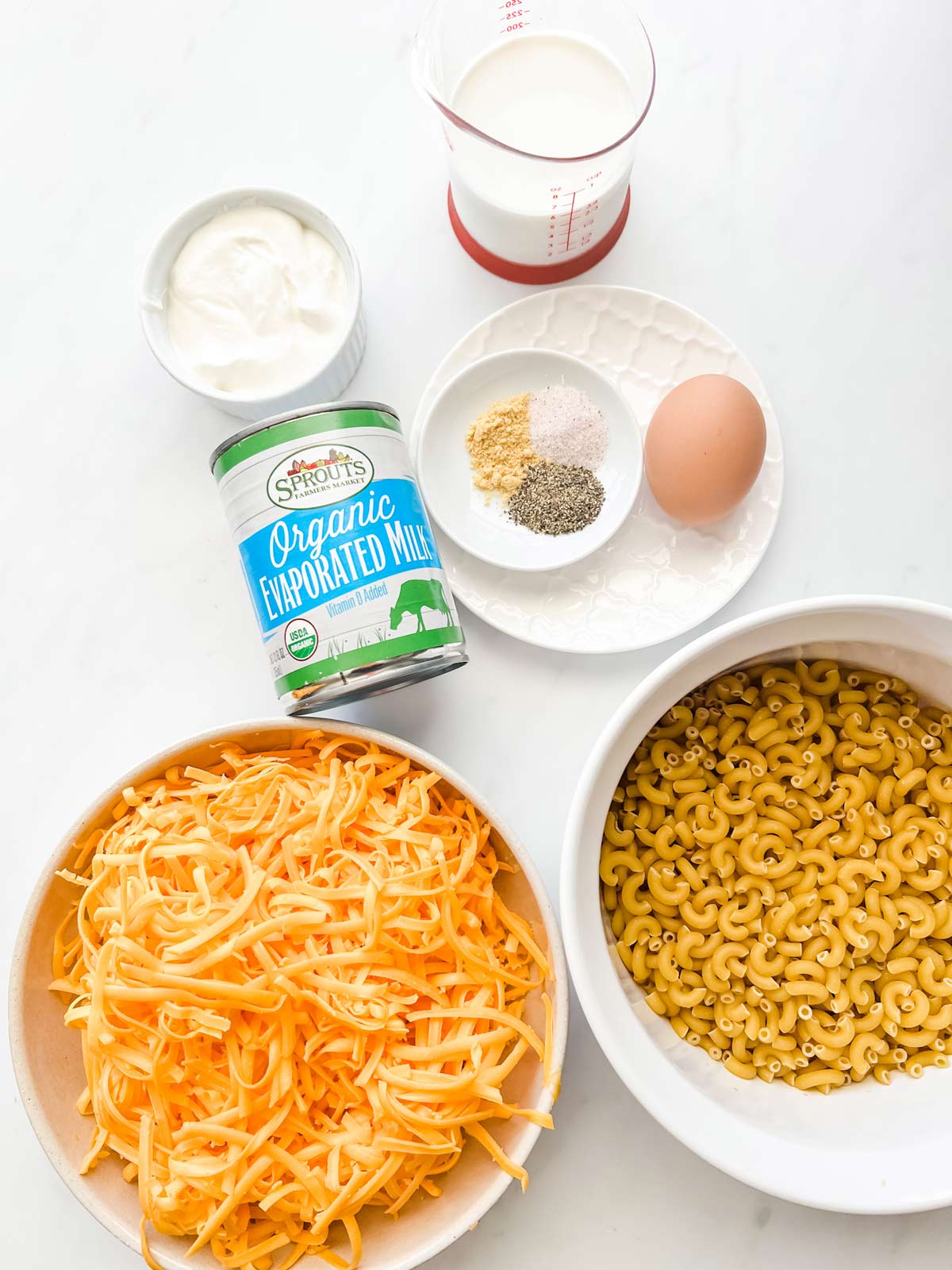 Overhead photo of elbow noodles, shredded cheese, evaporated milk, egg, seasonings, cream, and sour cream.