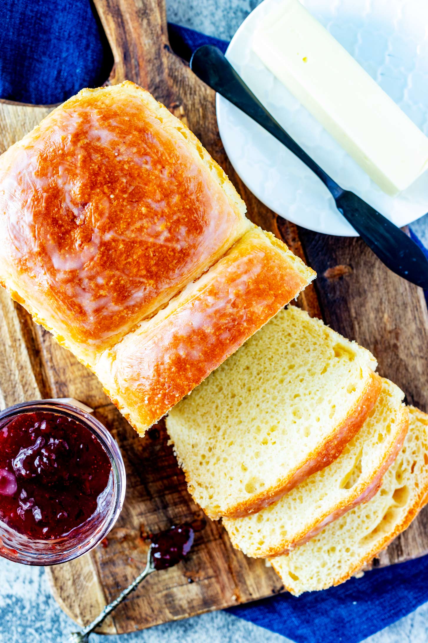 Partially sliced brioche bread on a cutting board with jam and butter next to it.