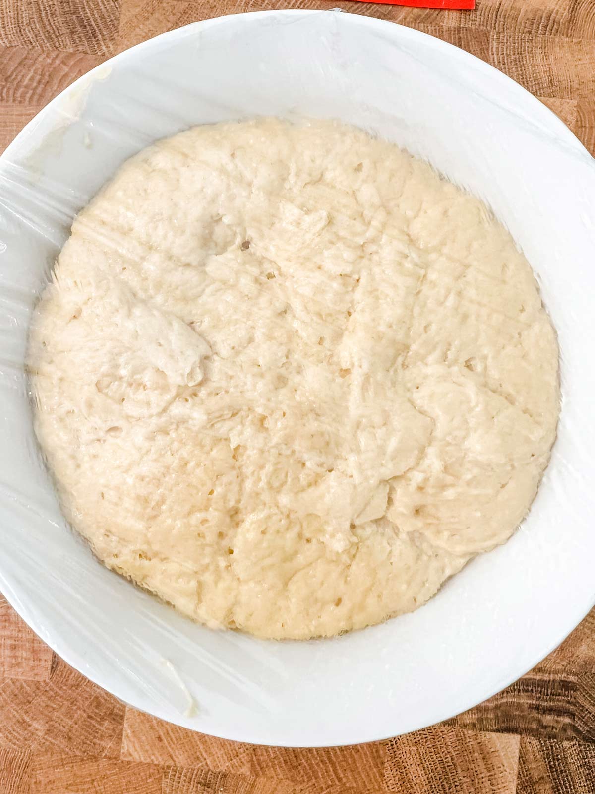 A white bowl with bread dough that has risen in the refrigerator.