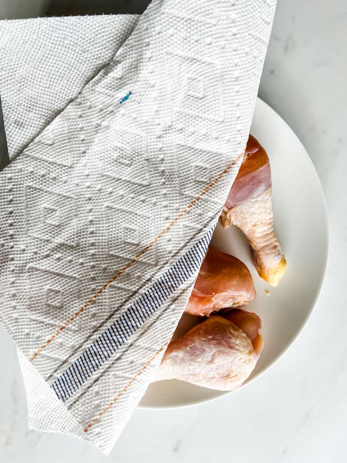 Chicken drumsticks being dried with a paper towel.