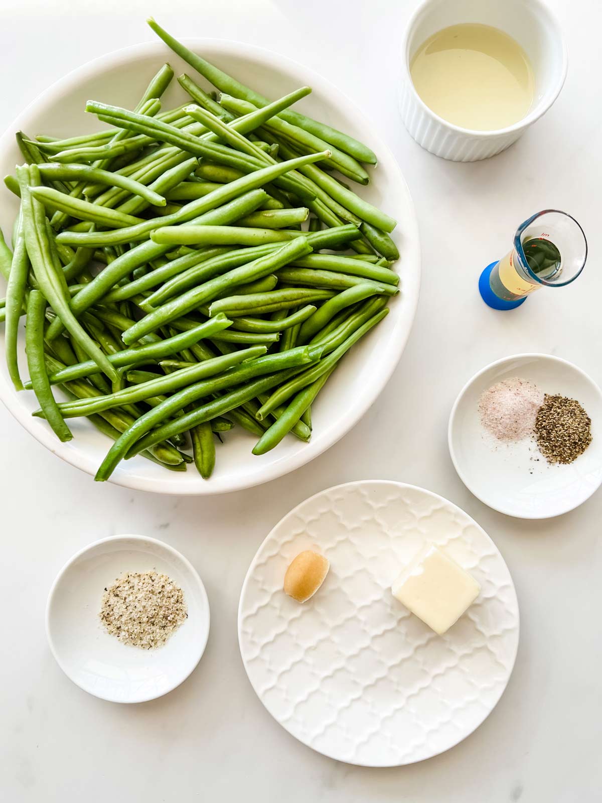 Overhead photo of fresh green beans, seasonings, butter, garlic, oil, and lemon juice.
