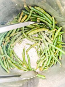Photo of green beans in the inner pot to an Instant Pot being tossed with lemon pepper.