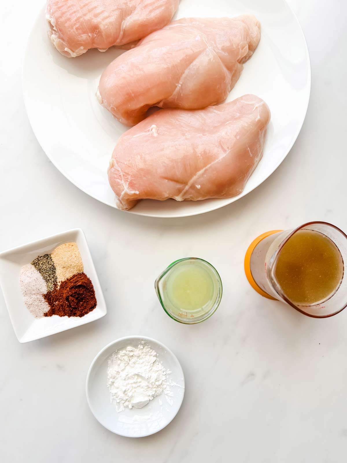 Overhead photo of a plate of chicken breast, seasonings, broth, lemon juice, and cornstarch.