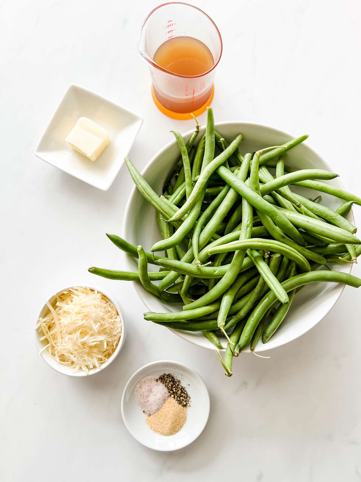 Overhead photo of green beans, broth, butter, parmesan, and seasonings.