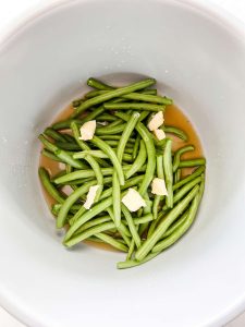 Green beans, broth, and butter in the inner pot of a Ninja Foodi.