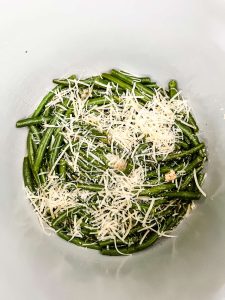 Photo of cooked green beans that have had parmesan cheese sprinkled on top in the inner pot of a ninja foodi.