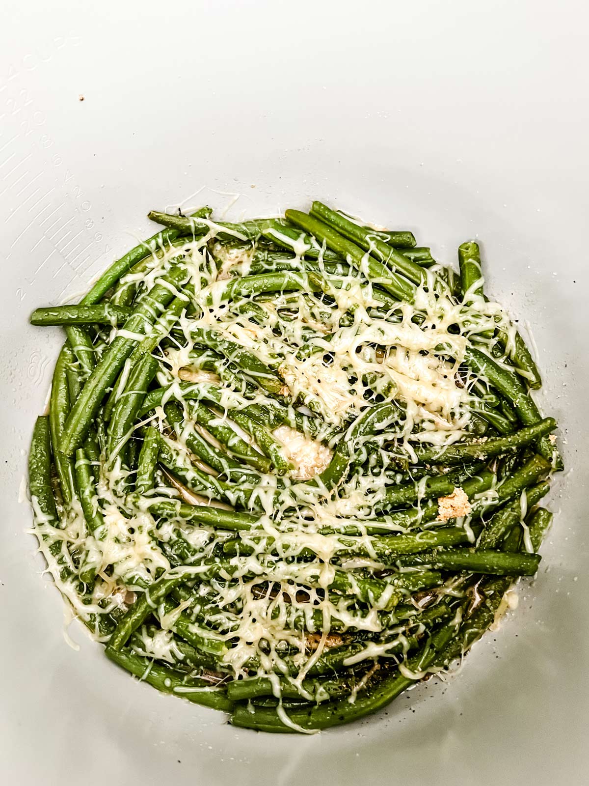 Green beans in the inner pot of a Ninja Foodi with parmesan cheese that has been melted on top using the air fry function.