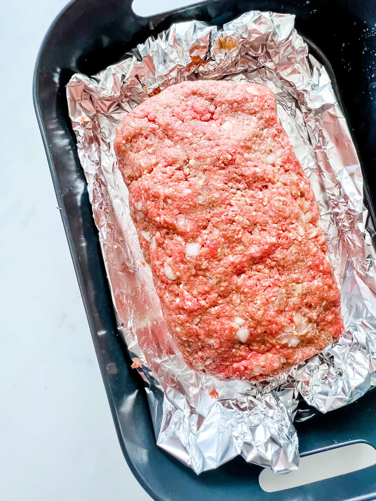 Meatloaf shaped on top of foil in an air crisp basket of a Foodi Grill.