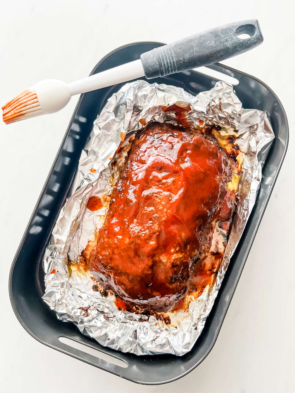 Meatloaf that has had glaze added on top in the air crisp basket of a Ninja Foodi Grill.
