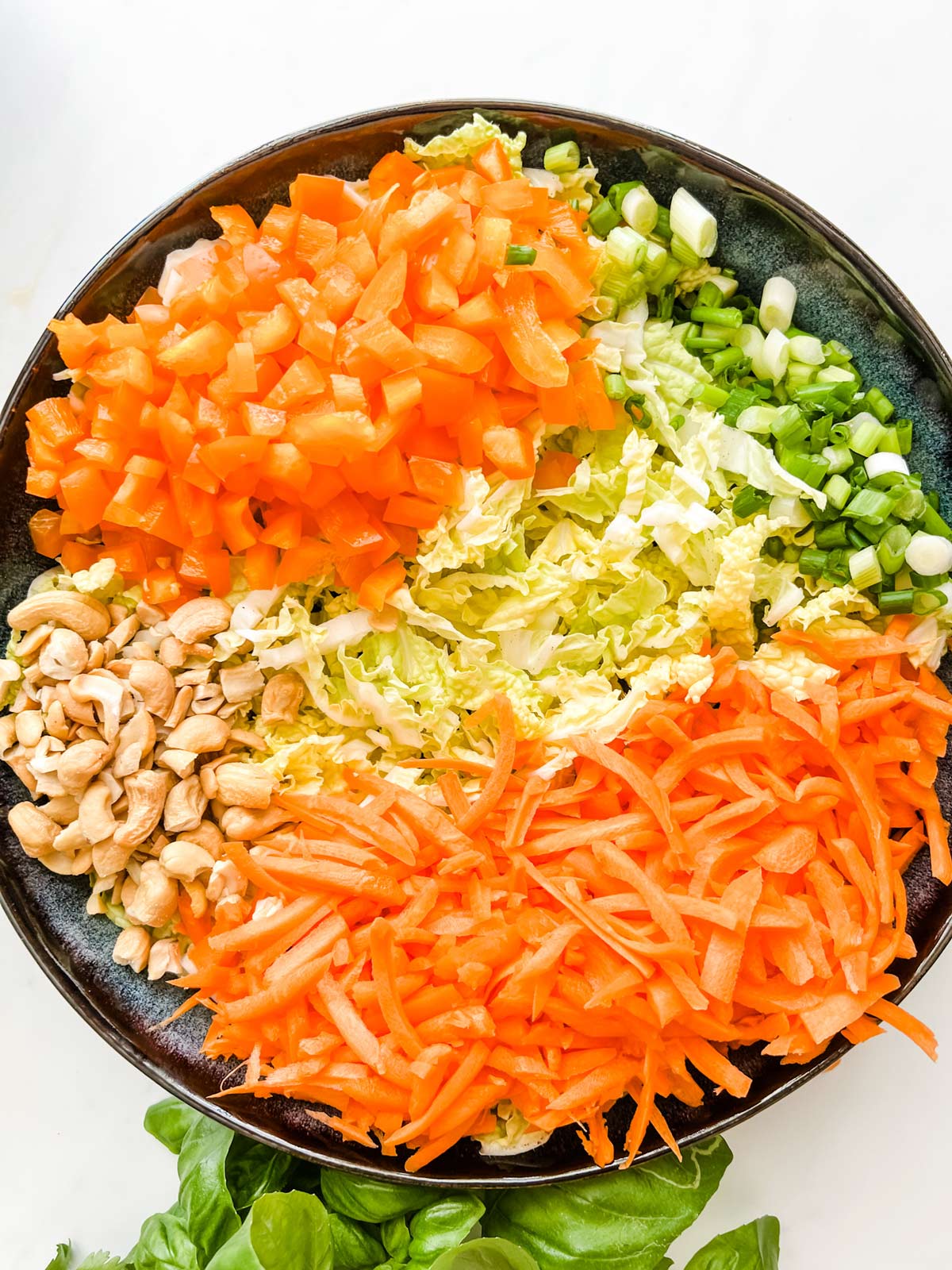 Chopped napa cabbage, bell pepper, green onion, carrots, and cashews in a large blue bowl.