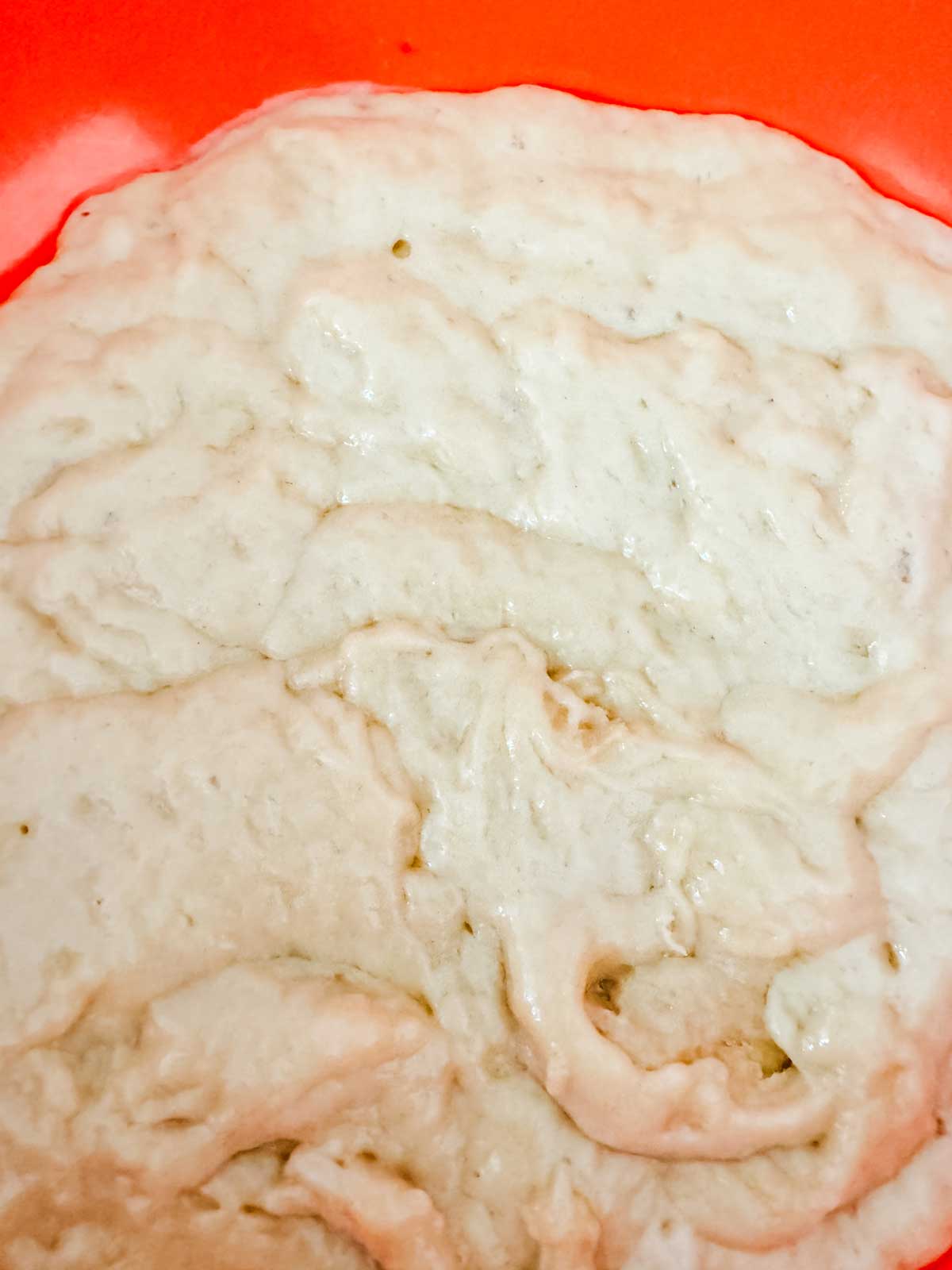 Wet brioche dough in an orange bowl ready for refrigeration.