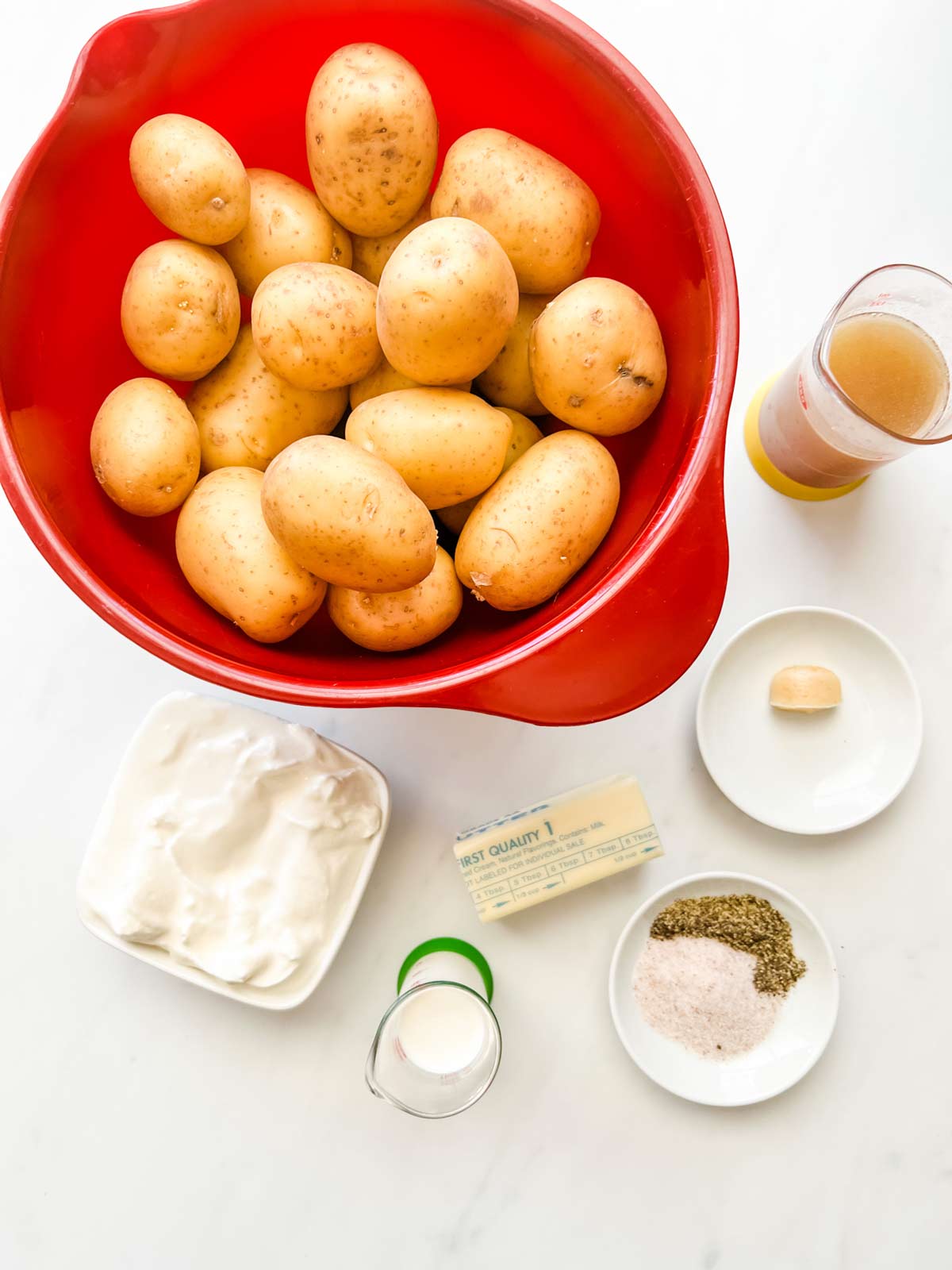 Overhead photo of potatoes, broth, sour cream, butter, cream, garlic, and seasonings.