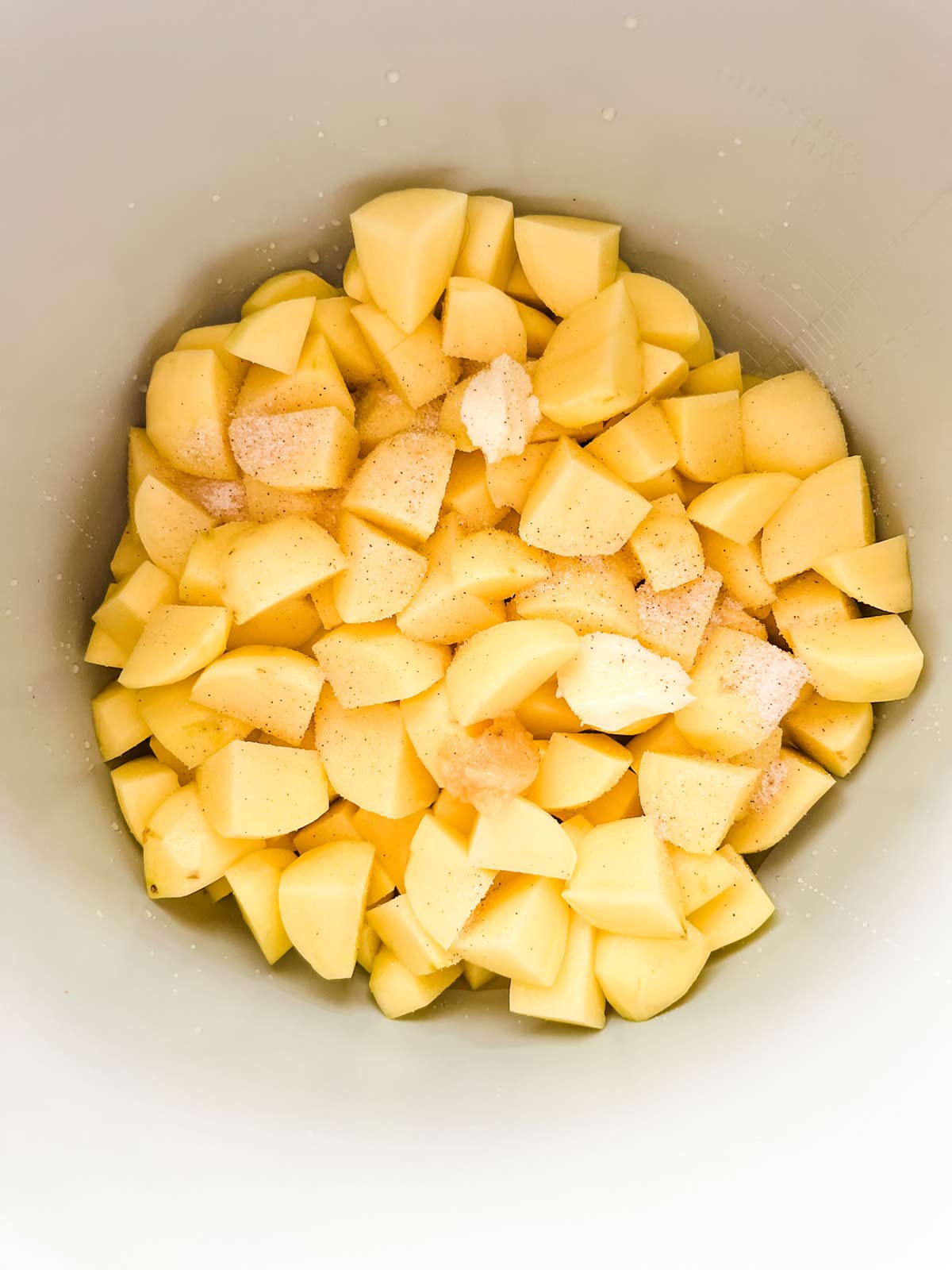 Cubed potatoes with garlic and seasonings in the inner pot of a Ninja Foodi.