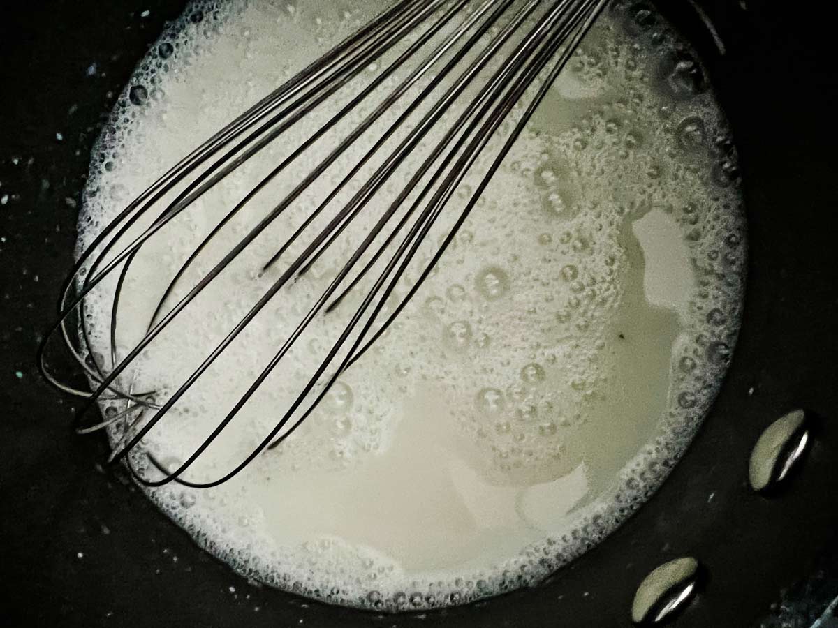 Milk, sugar, and salt being whisked together in a skillet over medium heat.
