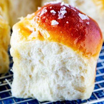 Close up photo of a bread machine dinner roll on a cooling rack with other rolls behind it.