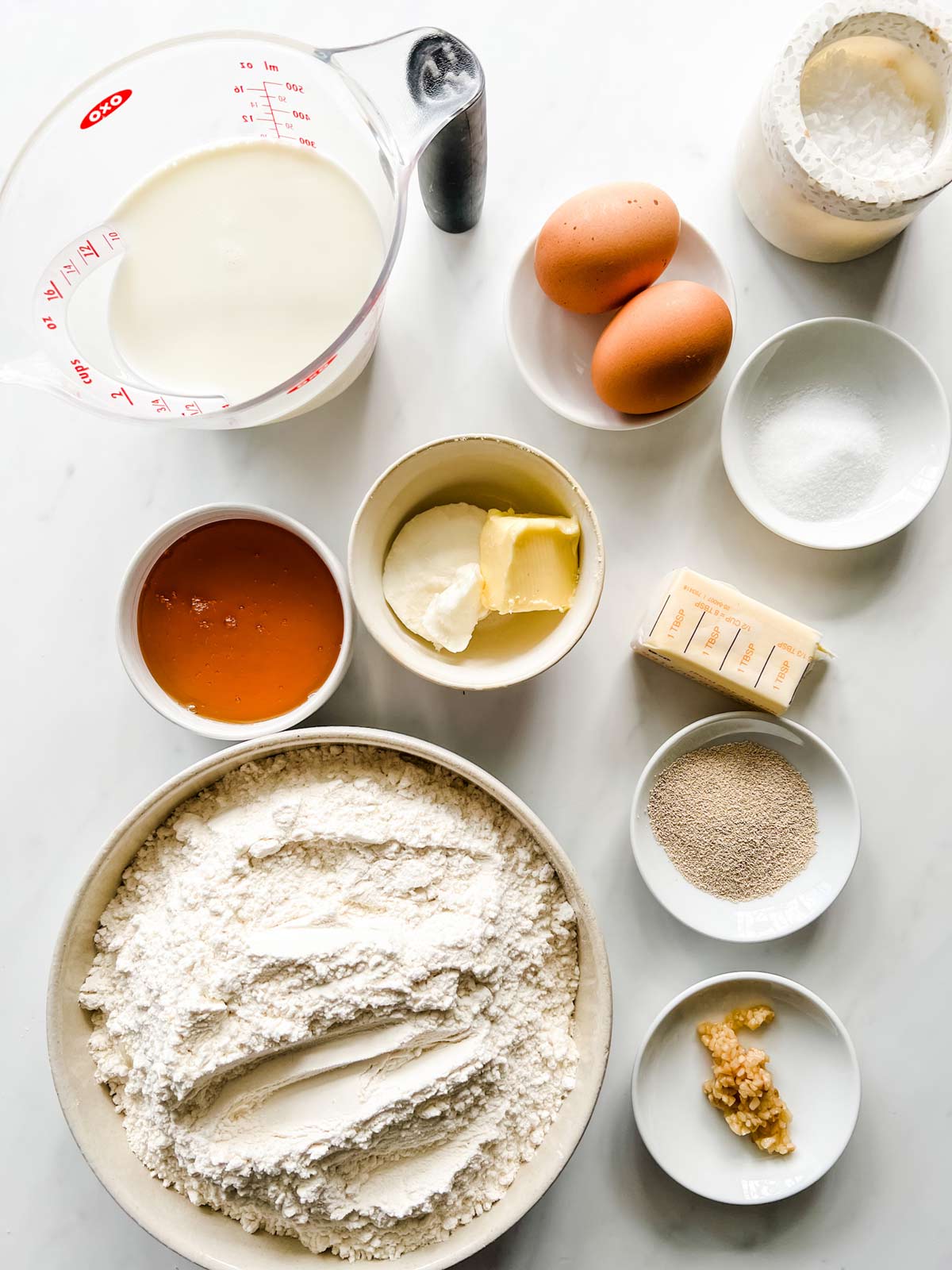 Overhead photo of milk, egg, honey, vegetable shortening, butter, salt, flour, yeast, and egg in prep containers.