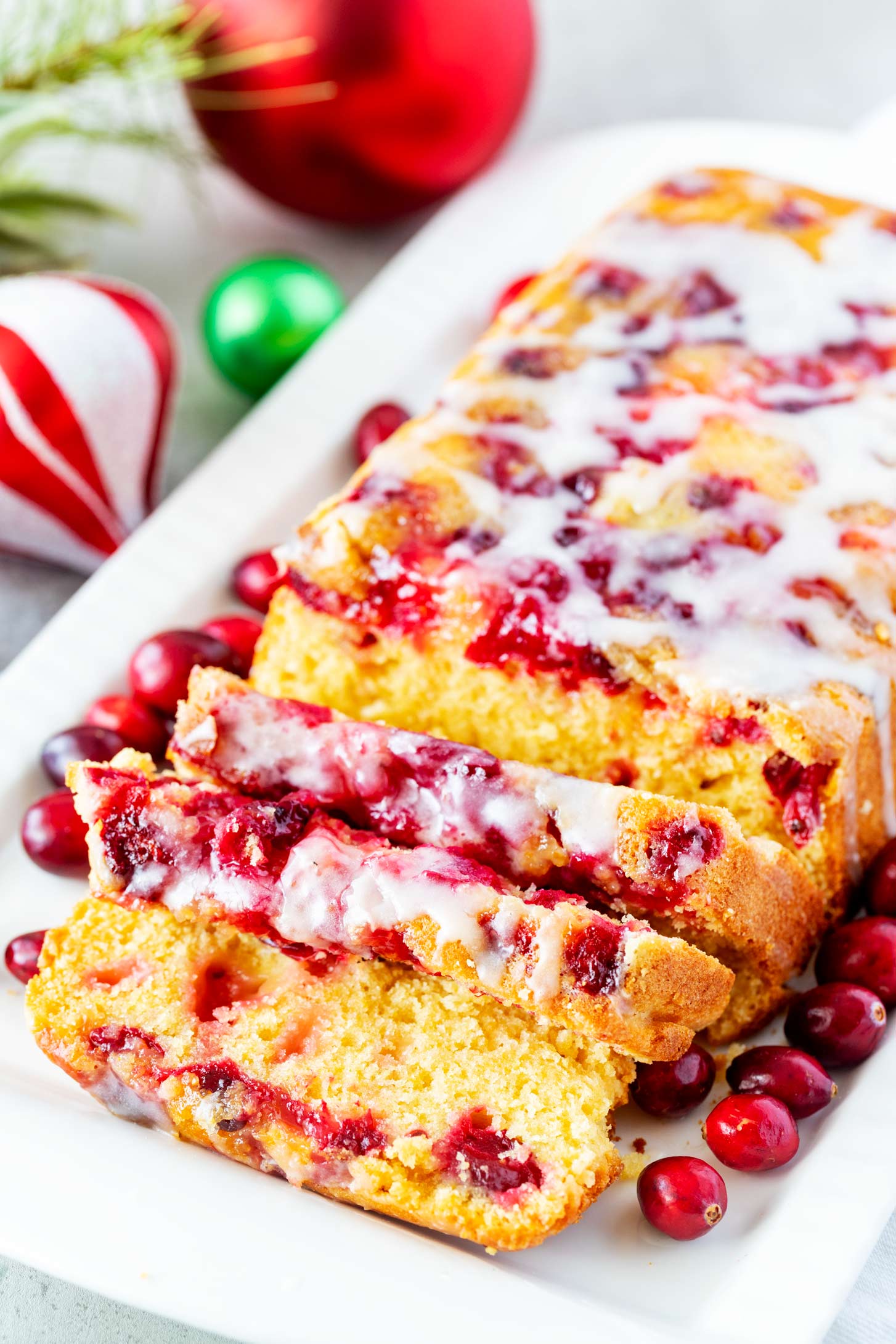 Close up photo of a white platter of a cranberry orange bread loaf with fresh cranberries on its sides.