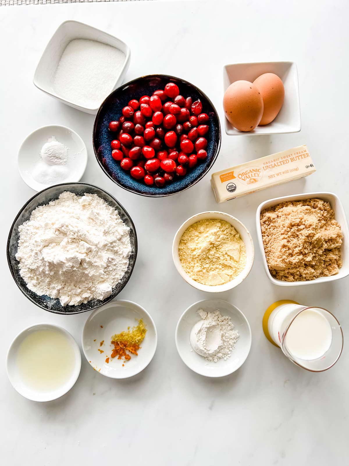 Overhead photo of cranberries, sugar, lemon and orange zest, flour, milk, cornmeal, brown sugar, baking powder, salt, butter and eggs.