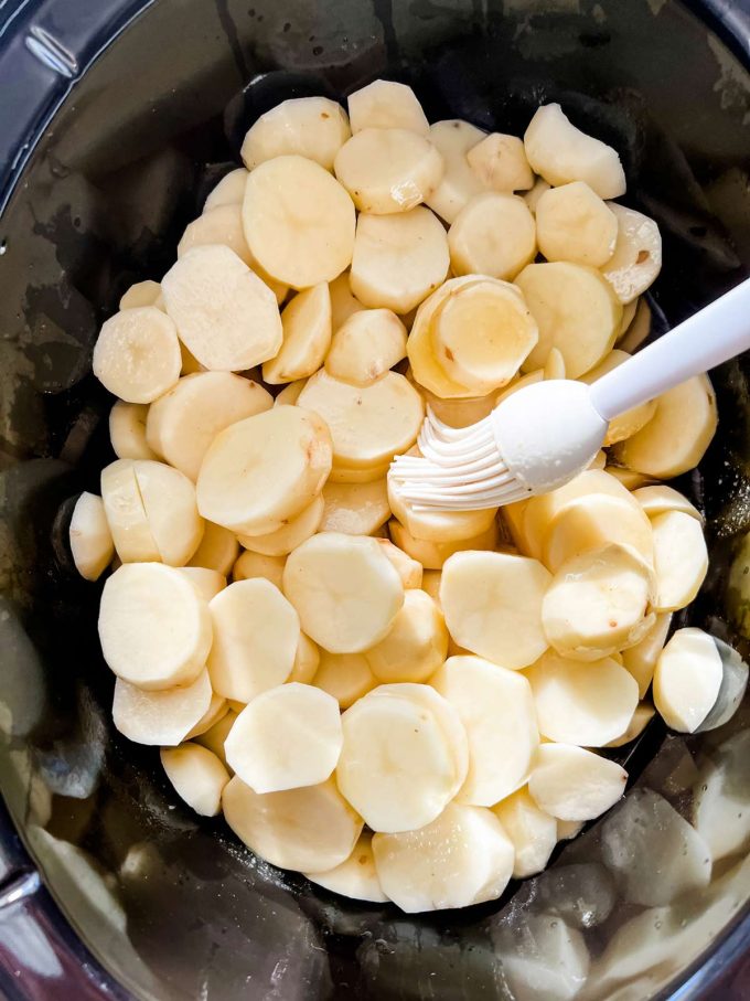 Photo of sliced potatoes in broth being brushed with oil.